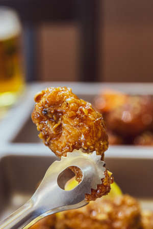 Close-up Golden Crunchy Korean Fried Chicken (basic Huraideu-Chikin) pinching with tong, served with pickled and Soju.の写真素材