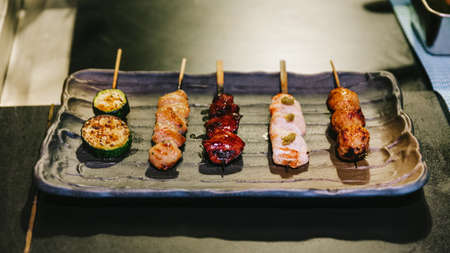 Yakitori (Japanese-Style Grilled Chicken Skewers) with chicken, internal organ and cucumber served on black stone plate.の写真素材