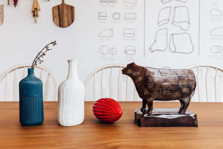 Wooden cow sculpture with cut of meat beef of diagram on it with blue, white jar and red fruit on wooden table.の写真素材