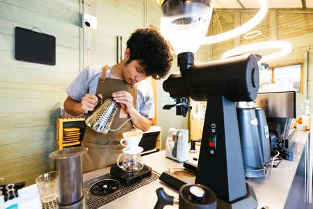 Barista making pour-over coffee with alternative method called Dripping. Coffee grinder, coffee stand and pour-over on a wooden table.のeditorial素材