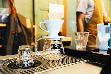 Barista making pour-over coffee with alternative method called Dripping. Coffee grinder, coffee stand and pour-over on a wooden table.の写真素材