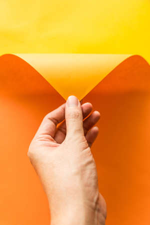 Hand pulling orange paper from yellow paper background. Abstract color paper background.の写真素材