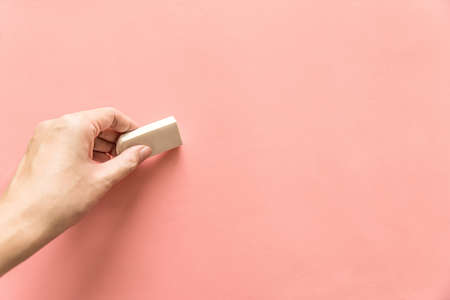 Hand holding white rubber for erasing something on empty pink background. Abstract background with copy space.の写真素材