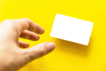 Foreground hand reaching empty white business card with shadow on yellow paper background.の写真素材