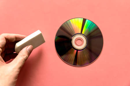 Hand pinching rubber over light reflected compact discs (CD) or digital versatile disc (DVD) on the pink paper background. Erasing data.の写真素材