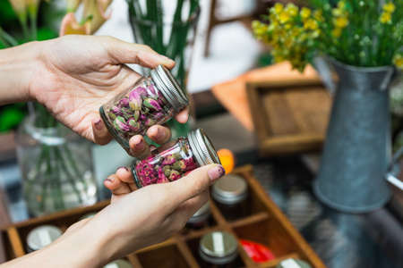 A woman choosing dry flowers for making flowering tea in glass bottles with aluminium lid on her...
