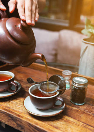 Hot Flower Tea served by pouring from mug through stainless steel tea strainer infuser in a brown porcelain cup.の写真素材