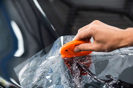 PPF installation process, close-up of hand cutting transparent film with orange color film cutter.の写真素材
