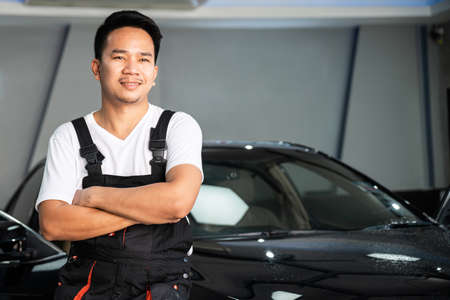 A Car Wrapping Specialist wearing car service costume standing and cross one's arm with the black car in the background. Auto car repair service center. Professional service.の写真素材
