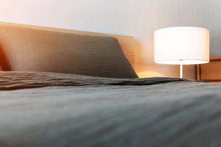 Bed with gray blanket and pillow with white electric lamp on the bedside table in bedroom interior....