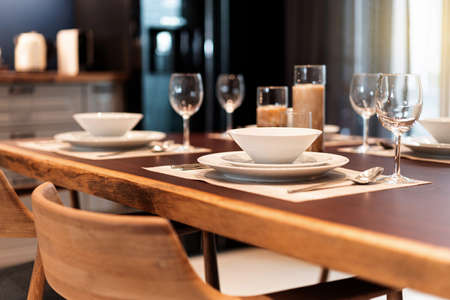 Elegant dinner table setting on a wooden table with dinnerware, silverware, utensil, wine glasses and candles. Table set for fine dining, luxury meal hotel service.の写真素材
