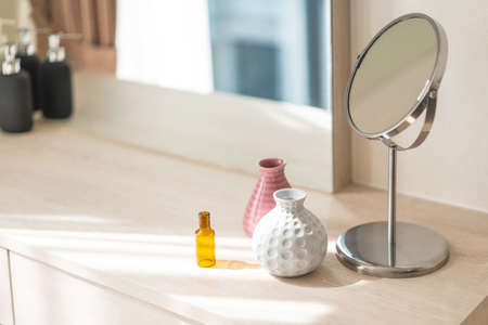 Dressing table with circle mirror, small flower vase in glossy ceramic white and pink vase and reagent bottle on the wooden counter for everyday skin care and cosmetic.の写真素材