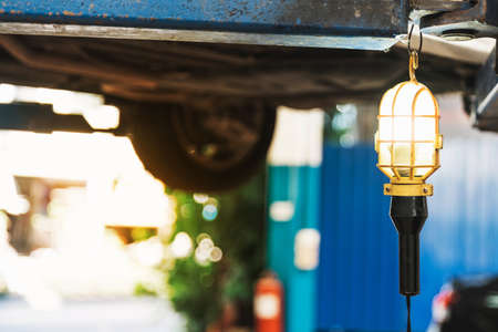 Portable hanging work lamp with energy saving bulb. Black and yellow colored plastic handle. Tool for professional car repair service.の写真素材