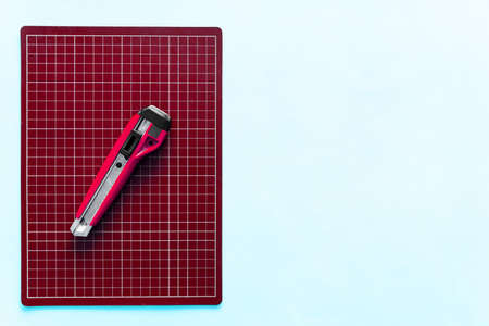 Top view of red rubber cutting mat with red cutter over pale blue color paper background. Background with copy space.の写真素材