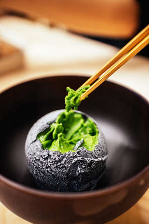 Charcoal coated a scoop of homemade green tea ice cream pinching with chopsticks in Japanese teahouse dessert cafe. Tasty exotic fusion dessert in Asian style.の写真素材
