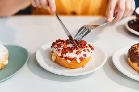 A woman wearing a yellow shirt cut a crispy bacon and cheddar cheese homemade donut with a knife and...