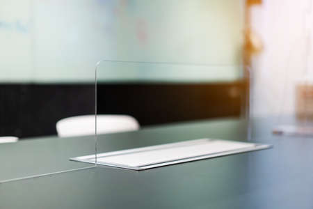 Close up of acrylic  separator standing partition wall with pass-through on the desk in the meeting room. Social distancing in offices during the Covid-19 pandemic. Precaution and safe.