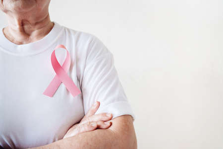 The senior woman supports Breast Cancer Day by stick Pink Ribbon Breast Cancer Awareness on her chest with copy space. Healthcare and medicine concept. October Pink day. World Cancer Day.の写真素材