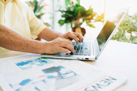 Close-up a senior retired old man using a laptop with hands pressing keyboard while sitting at home....