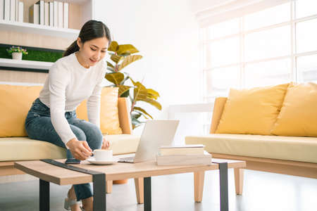 Asian woman sitting and working on the sofa. Business woman working on laptop at home. Woman working in a relax area in the office. Business quarantine period.の写真素材