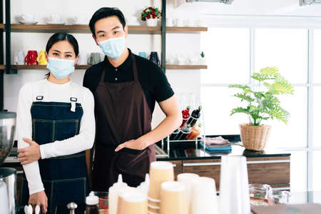 Young male and female barista wearing a face mask standing inside the coffee counter. Coffee making classes for entrepreneurs to start a small business. People's lifestyles during Covid-19 pandemic.の写真素材