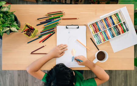 Top view of the child's drawing with colored pencils on white paper on a wooden table. Children's...
