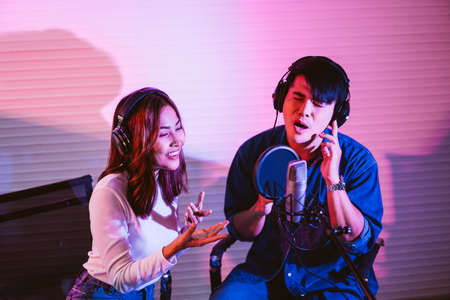 Asian male and a female vocalist singing in the studio in a rehearsal session. Performance and show in the music business. Image with copy space. Small and home recording studio.の写真素材