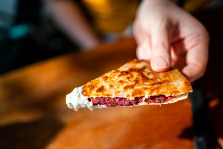 Hand holding Vegan Quesadilla: grilled whole-wheat tortilla filled with sweet potato and red bean, vegan quesso cheese dipped with Tzaziki sauce. Creative Mexican vegan food.の写真素材
