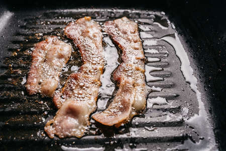 Close-up frying sizzling bacon strips in a pan with hot greasing bacon oil for making crispy bacon. with copy space. Keto snack meal.の写真素材