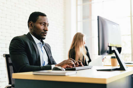 The African businessman typing keyboard and looking on the screen with intention at his desk workplace with copy space.の写真素材