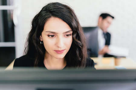 Close-up portrait of a Caucasian businesswoman typing and looking on a computer screen with intention at her desk. Concern and fix problems in a corporate office.の写真素材