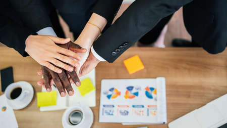 Diversity of African and Caucasian business people join hands together over the table during their meeting. Teamwork joins hands for support together. Strength, unity and success of corporate concept.の写真素材