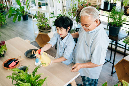 An Asian retired grandfather and his grandson spend quality time together at home. Enjoy taking care by watering plants. The family bond between children and adultsの写真素材