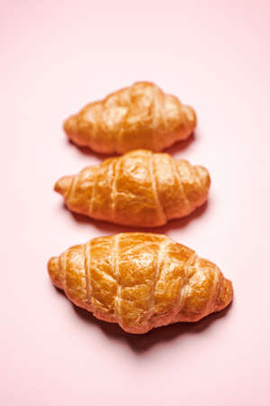 Three fresh-baked crispy golden buttery croissants isolated on pink background with copy space. Pastry and dessert studio shot.の写真素材