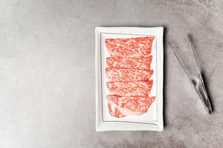 Top view of premium rare slices sirloin Wagyu A5 beef with high-marbling texture on a ceramic plate with bbq tongs, Served for Yakiniku, Sukiyaki and Shabu. Image with copy space.の写真素材