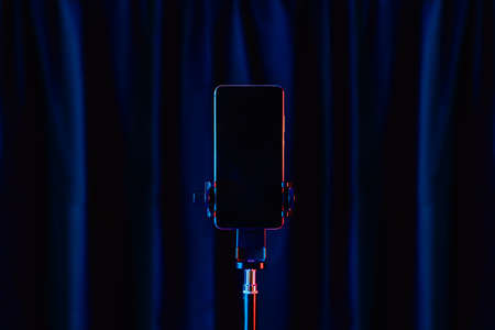 Clipping path display of vertical mobile phone with stand in blue and red lights with black curtain background with copy space. Mobile live performance and show in the live business equipment.の写真素材