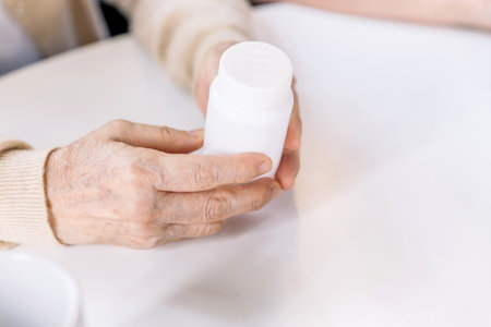 Close up hands of a senior woman holding a medical bottle and asking for information from the nurse before administering medication. Caregiver visit at home. Home health care and nursing home concept.の写真素材