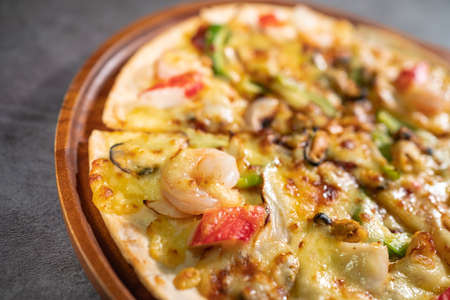 Close up of tasty hot baked seafood crispy pizza - mussels, shrimps and kani with chili pepper and melted mozzarella cheese on round pizza dough, on a wooden pizza pan over the concrete table top.の写真素材