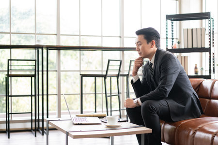 Asian businessman executive manager looking at a laptop computer, thinking about stock and crypto market volatility or meeting an online webinar and waiting for the decision in the office.の写真素材