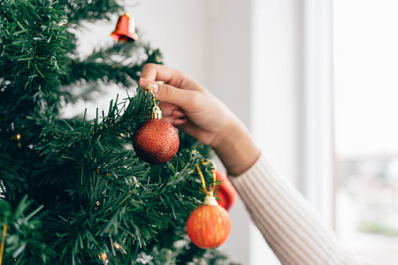 Close up woman's hand touching and decorating a red bauble on the Christmas tree in the living room at home. Enjoying and celebrating the Christmas holiday.の写真素材