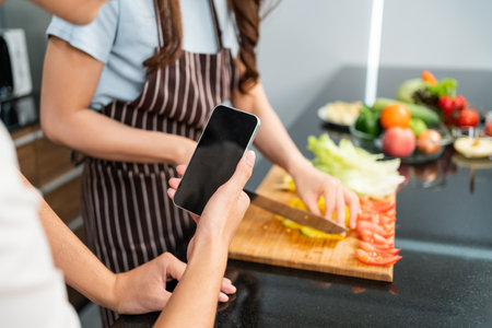Close up hands of man live by mobile phone during woman prepare a vegetarian healthy salad with fresh vegetables such as carrot, tomato cabbage and green oak in the home kitchen.の写真素材