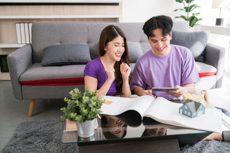 Young happy loving couple talking and using tablet to calculate the price of buying a house with a...