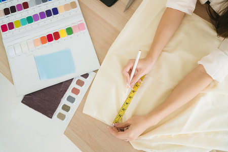Top view of female fashion designer or tailor hand measuring fabric with measuring tape with example...