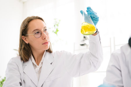 Caucasian woman scientist researcher wearing eye glasses shaking substance in the conical flask for...