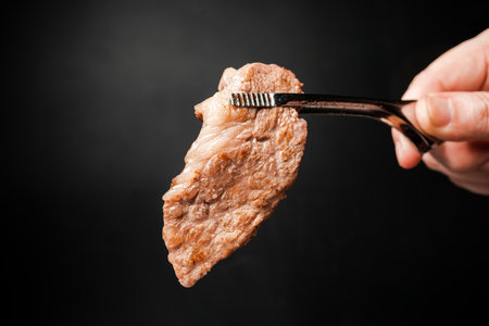 A medium rare piece of high marble Sirloin A5 Wagyu picked and grilled on a marbled pan with BBQ tongs on a black background. Yakiniku and beef grill concept.の写真素材