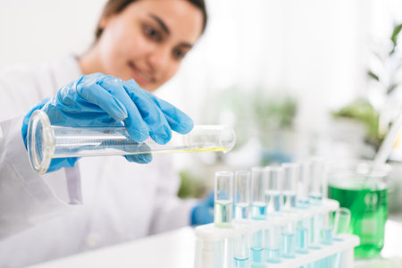 Middle East woman scientist researcher rinse liquid from a graduated cylinder to test tube for...