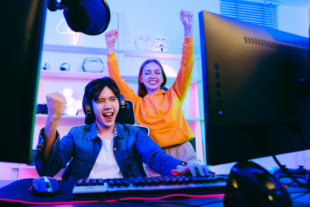 Asian male gamer and Caucasian woman coach celebrating victory together in front of the gaming table. Gamer winning an esports game with mentor. The player rejoices in victory in the competition.の写真素材