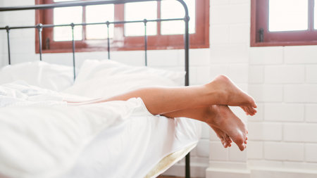 Feet of happy two friends Caucasian young women in white bathrobes lying on the bed at home. LGBTQ...