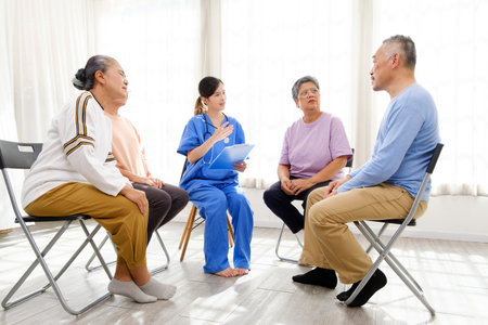 The caregiver therapist sits with a group of Asian senior people in a circle for checking physical and mental health in a group elderly therapy session. The nursing home facilitates a support groupの写真素材