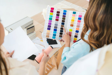 Two Asian female fashion designers or dressmakers brainstormed and discuss the design of the new collection with samples of fabrics and sketches on the tablet. Working together in the studio.の写真素材